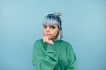 Pensive young lady with blue hair stands on a colored background and looks into the camera with a serious face. Isolated.