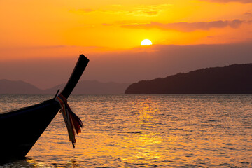 Silhouette Long Tail Boat in the tropical sea at golden sunset, mountains and orange sky with clouds