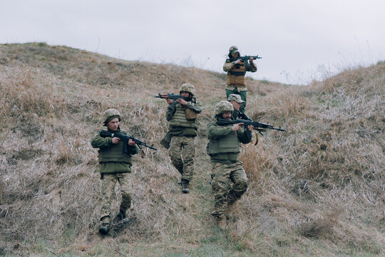 Team of five Ukrainian soldiers aims from kalashnikov assault rifles to russian enemy against background of hill.