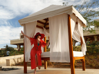 Summer vacation woman in red hat and cape for the beach with mobile phone near gazebo and palms,...