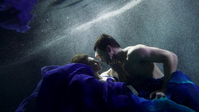 romantic love story underwater, young man and woman are embracing and floating in water of pool