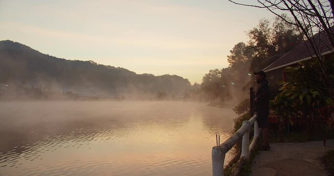 Asian tourist traveler man standing enjoy vacation holiday trip against sunrise in the morning at lakeside ban rak thai village, Mae Hong son Thailand, travel summer adventure journey in nature