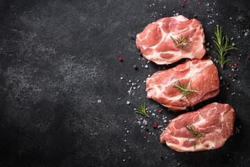 Fresh pork steaks with spices at black background. Top view with copy space.
