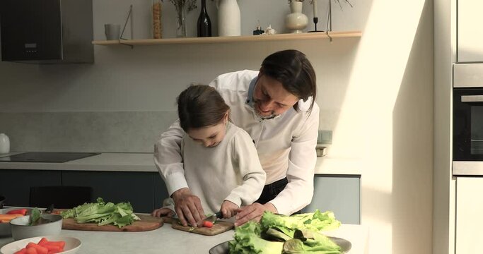 Loving single dad teach daughter preschooler to cook simple healthy meal take care of child safety at kitchen. Smart little girl hold knife learn to cut carrot for vitamin salad under father control