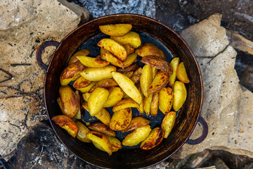 Homemade crispy potatoes on a frying pan on the fire outside. Picnic in nature with cooking.