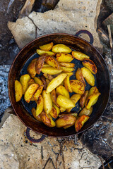Homemade crispy potatoes on a frying pan on the fire outside. Picnic in nature with cooking.