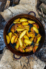 Homemade crispy potatoes on a frying pan on the fire outside. Picnic in nature with cooking.