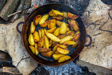 Homemade crispy potatoes on a frying pan on the fire outside. Picnic in nature with cooking.