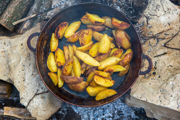Homemade crispy potatoes on a frying pan on the fire outside. Picnic in nature with cooking.