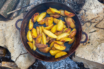 Homemade crispy potatoes on a frying pan on the fire outside. Picnic in nature with cooking.