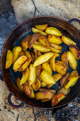 Homemade crispy potatoes on a frying pan on the fire outside. Picnic in nature with cooking.