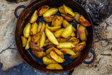 Homemade crispy potatoes on a frying pan on the fire outside. Picnic in nature with cooking.