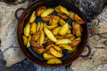 Homemade crispy potatoes on a frying pan on the fire outside. Picnic in nature with cooking.