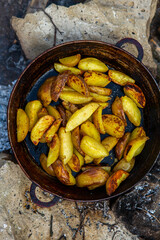 Homemade crispy potatoes on a frying pan on the fire outside. Picnic in nature with cooking.