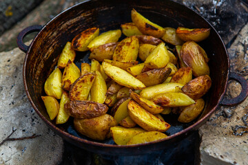 Homemade crispy potatoes on a frying pan on the fire outside. Picnic in nature with cooking.