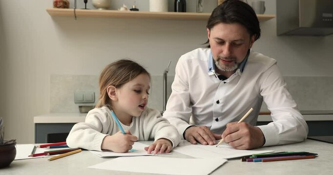 Caring dad teach small daughter to draw with colored pencils create fairy tale character picture on paper make up funny story for kid. Adorable girl spend good time for painting with father at kitchen