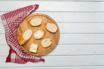 Fresh baguette with butter on a round board on a white background