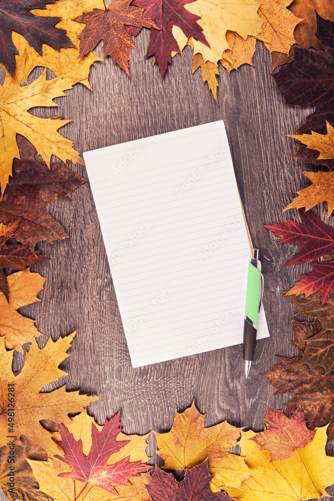Wall mural autumn leaves and notepad disposed on wooden table in the background. view from above.