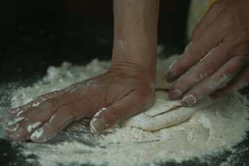 Fototapeta premium The cooking process of a bread dough. Baking bread recipe. Bakery breads food, detail view with woman hands working on dough at an old wood pan. flour falling on a dark table. detail.
