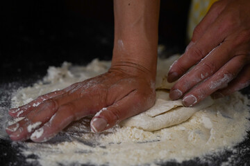 Fototapeta premium The cooking process of a bread dough. Baking bread recipe. Bakery breads food, detail view with woman hands working on dough at an old wood pan. flour falling on a dark table. detail.