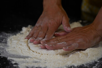 The cooking process of a bread dough. Baking bread recipe. Bakery breads food, detail view with woman hands working on dough at an old wood pan. flour falling on a dark table. detail.