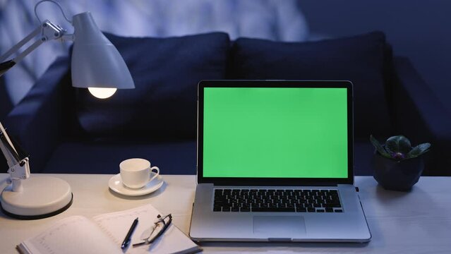 Close up zooming shot of modern chroma key green screen laptop computer set up for work on desk at night. Remote work, technology concept 4k uhd video template