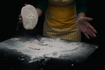 The cooking process of a bread dough. Baking bread recipe. Bakery breads food, detail view with woman hands working on dough at an old wood pan. flour falling on a dark table. detail.