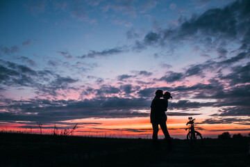 Fototapeta premium A couple kisses and hugs in a field at sunset, next to a bike
