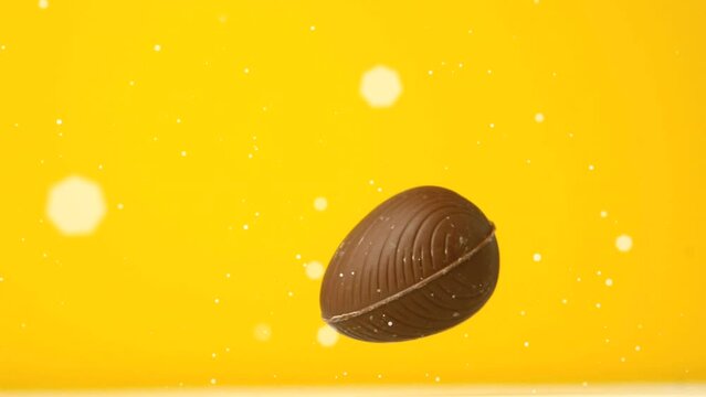Animation of white spots floating over chocolate easter egg falling and bouncing, on yellow