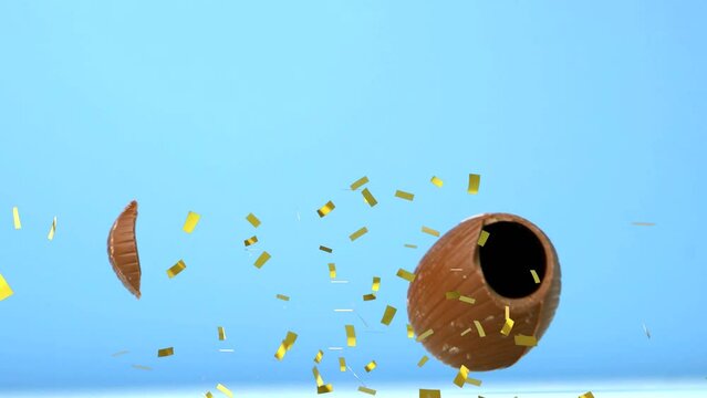 Animation of gold confetti falling over chocolate easter egg falling and breaking, on blue