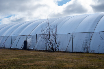 The exterior of a white semi permanent indoor tennis court dome tent. The polythene symmetrical...