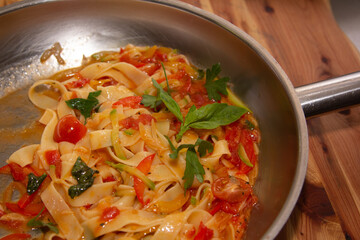 The chef prepares Pappardelle or Linguini pasta in tomato sauce in a steel pan.