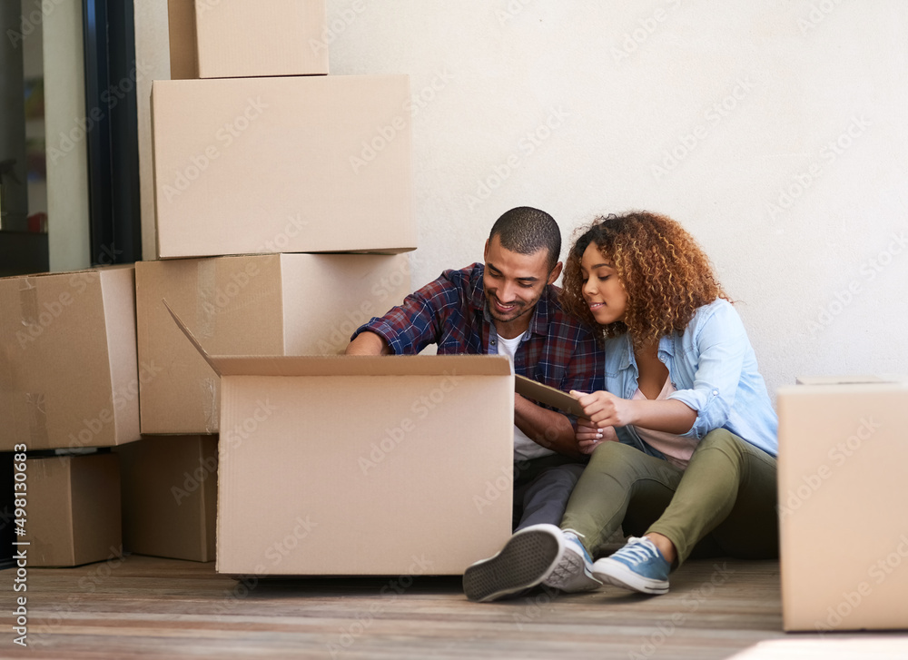 Poster whats in the box. shot of a young couple unpacking a box together while sitting on the floor of thei