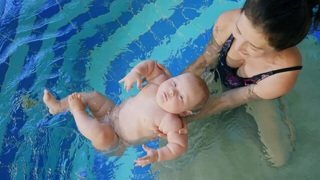 Happy mother in red swimming suit with baby son surfing water with fun in swimming pool. Healthy lifestyle, active parent, swimming lessons in indoor swimming pool with child, little fun kid on