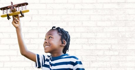 African american boy playing with a toy plane against copy space on grey brick wall background © vectorfusionart