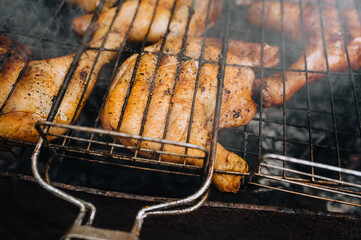 Large pieces of chicken thighs are fried on the grill in a barbecue on a fire with smoke in nature.