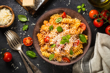 Italian pasta alla arrabiata with basil, tomato and parmesan on dark table. Top view image.