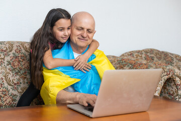 Grandfather and granddaughter with laptop and flag of Ukraine