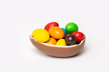 Cracked chocolate easter egg with colorful small round candies on white background, copy space, side view. Chocolate treat for kids. Easter concept.
