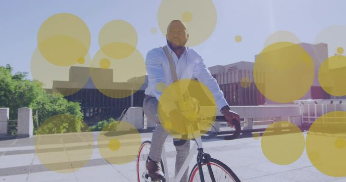 Animation of yellow dots over african american businessman riding on bike in city