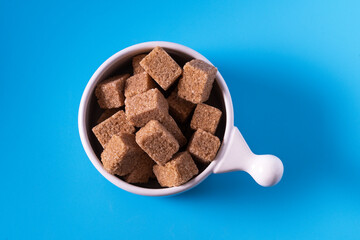 Brown raw sugar demerara in a white cup, on blue background, top view.