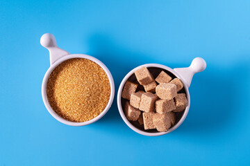 Top view different types of brown raw sugar in bowls on a blue background.
