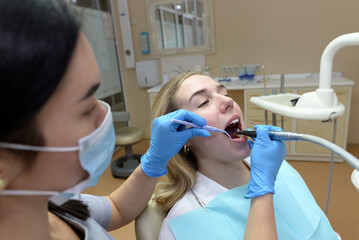 Dentist woman treats the teeth of a young patient with the help of professional dental instruments.