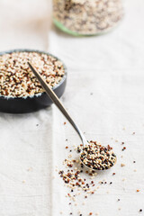 Mix of raw white, red and black quinoa in a bowl and in a spoon on a cloth. Healthy gluten free food. Vertical view