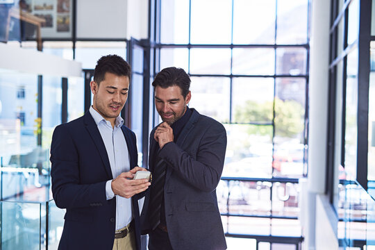 The client texted some great feedback on our latest deal.... Cropped shot of two businessmen discussing something on a cellphone in an office.