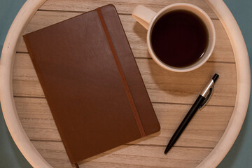 A cup of black coffee, pen and notebook lying on the wooden table