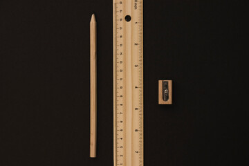 Wooden pencil, ruler and pencil sharpender lying on the black paper background in the middle