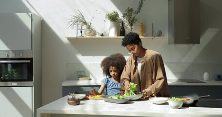 Happy Black mom elder grownup sister show little preteen age girl how to cook tasty salad. Smart tween daughter assist mother at kitchen learn family recipe of healthy food delicious vegetarian course