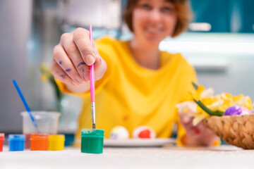 Close up of female hands paintings eggs to the Easter. Blurred smiling woman at the background. Concept of Easter holiday