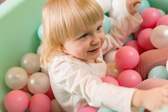 A little cheerful girl is playing in dry pool with colorful balls. Smile. Close-up